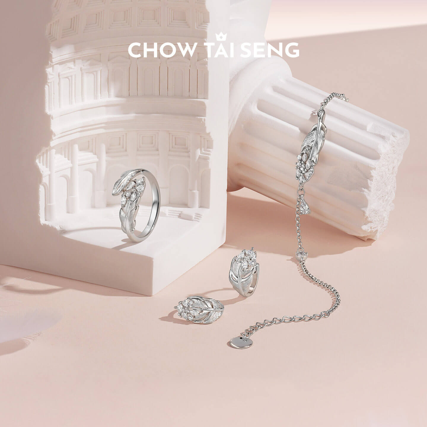 ChowTaiSeng sterling silver swan feather jewelry set styled with matching ring, stud earrings and chain bracelet on white architectural prop with peach background