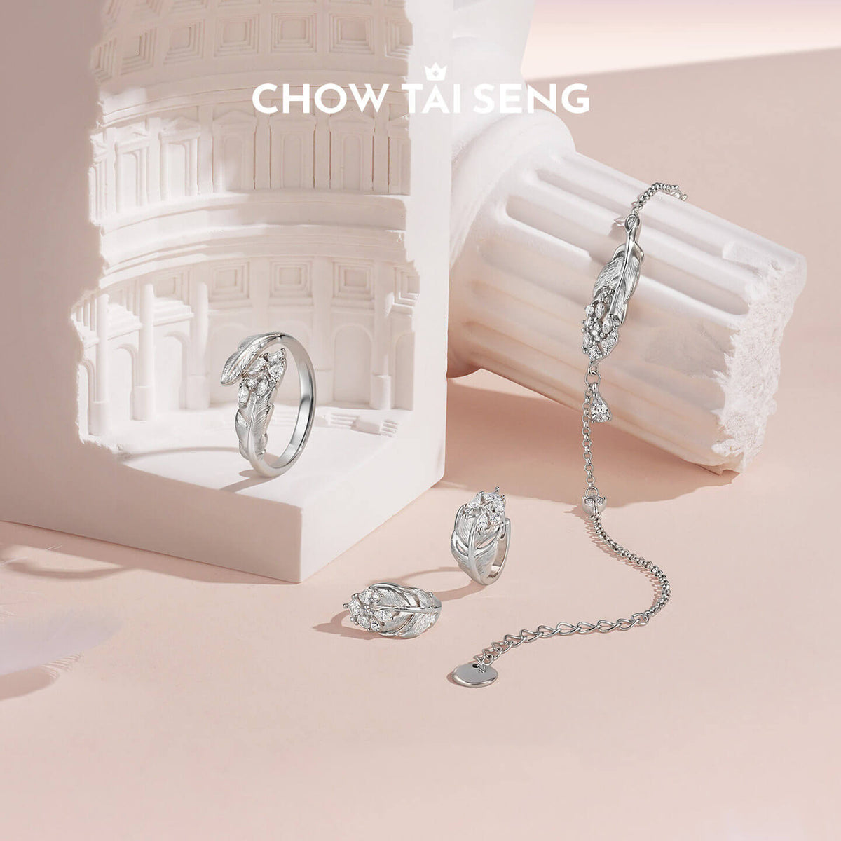 ChowTaiSeng sterling silver swan feather jewelry set styled with matching ring, stud earrings and chain bracelet on white architectural prop with peach background