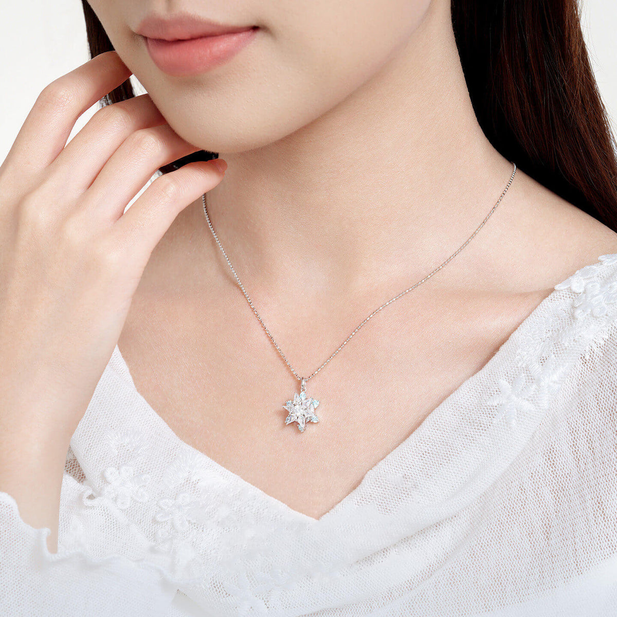 Model wearing ChowTaiSeng S925 silver snowflake necklace — rotating CZ pendant on box chain, white lace top, side neck view with hand pose