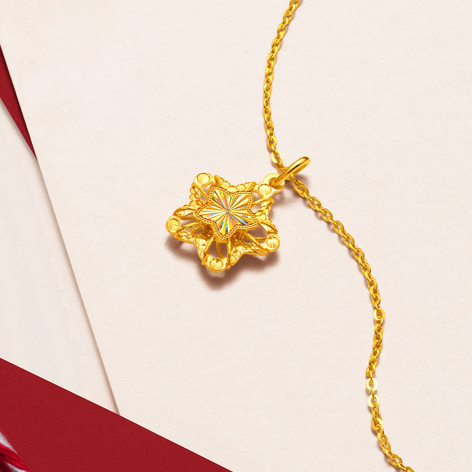ChowTaiSeng 24K gold wishing star pendant — angled flat lay on cream paper with red ribbon accent, hollow filigree star with iridescent laser-engraved centre, cable chain
