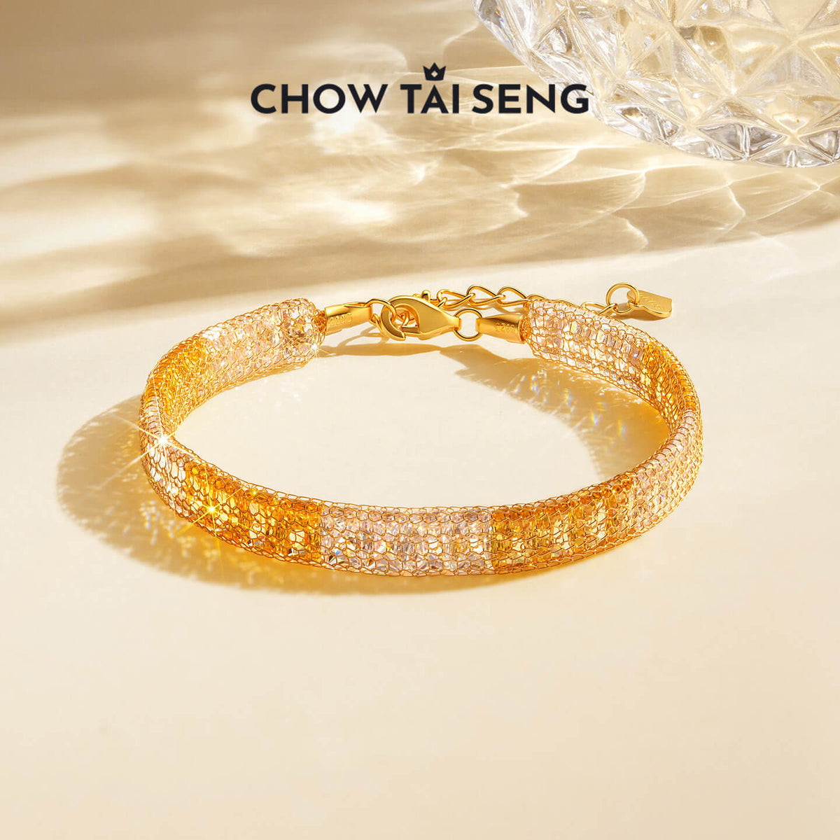 ChowTaiSeng two-tone gold-plated silver mesh bracelet with cubic zirconia in sunlight beside faceted glass