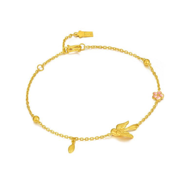 Angled view of a 24K gold magpie bracelet with a pink enamel plum blossom, dangling leaf and clasp