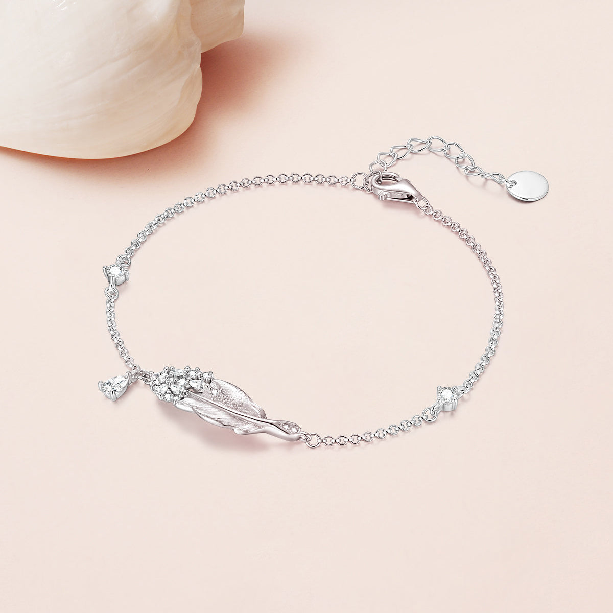 925 sterling silver swan feather bracelet with CZ cluster and teardrop drop charm, styled on pink surface with white shell prop