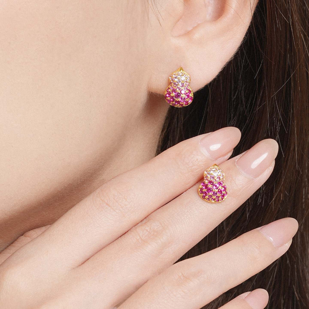 Close-up of a pink gemstone gourd stud earring worn on the ear