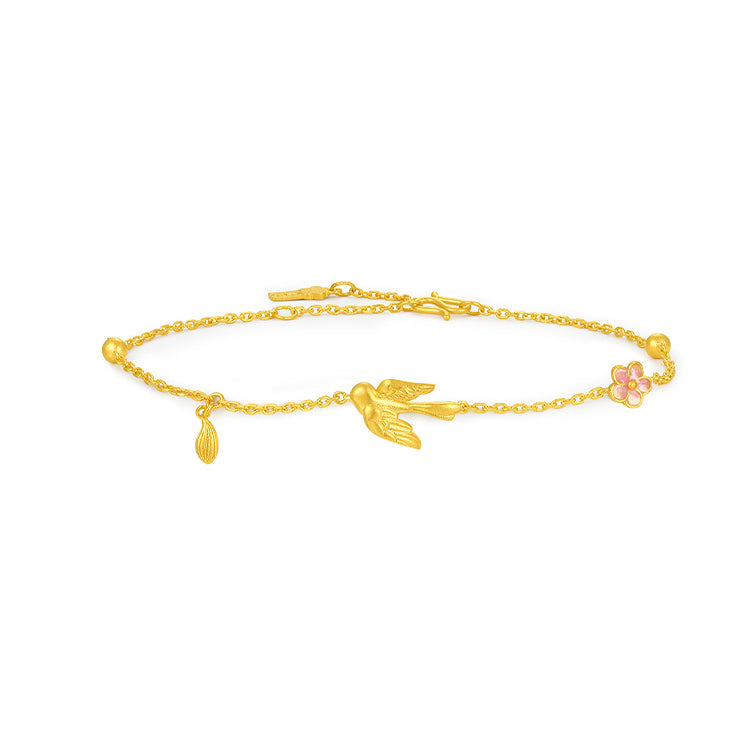24K gold bracelet in a low-angle view showing a sculpted magpie, pink enamel plum blossom and leaf charm