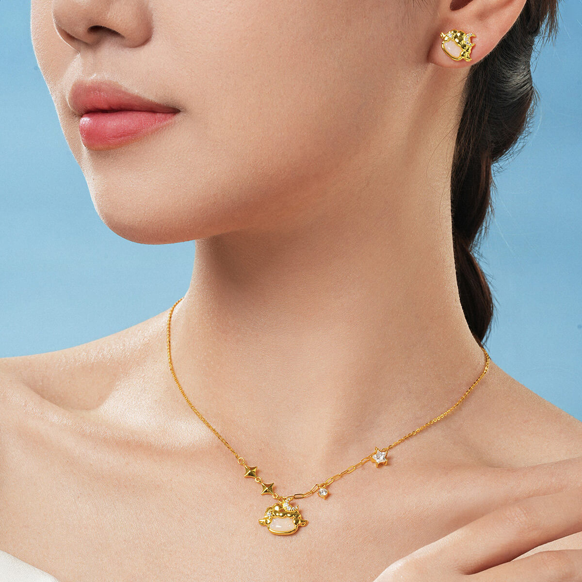 Model wearing gold-plated silver chalcedony sheep necklace and matching stud earrings against a blue background