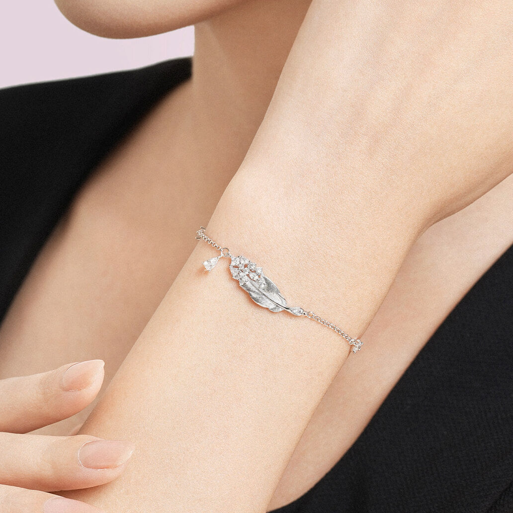 Woman wearing 925 sterling silver swan feather bracelet with cubic zirconia cluster charm on wrist, on-model lifestyle close-up