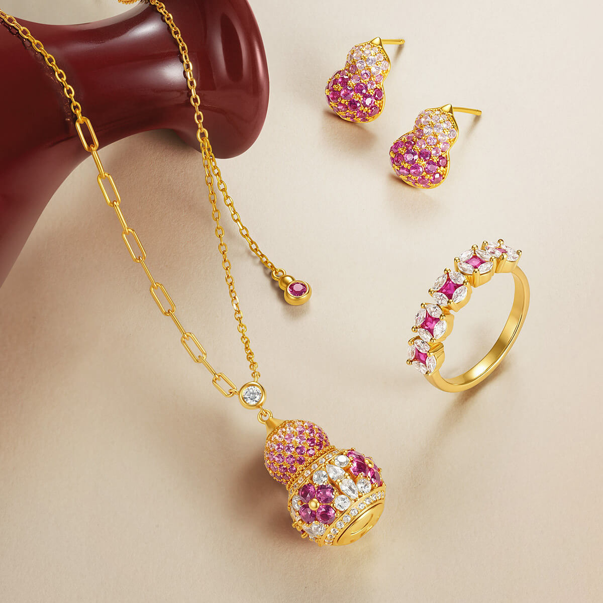 Gold-plated silver pink gourd necklace and stud earrings displayed beside a coordinating gemstone ring