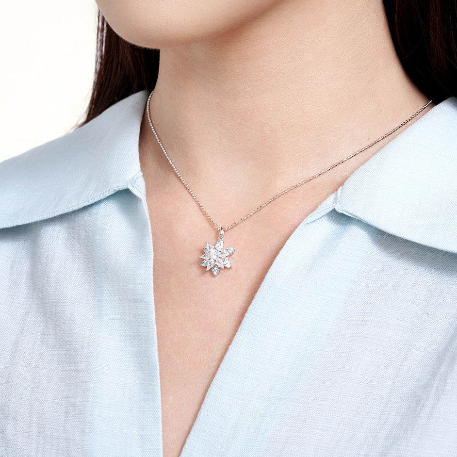 Model wearing ChowTaiSeng S925 silver snowflake necklace — rotating CZ pendant on box chain, blue shirt V-neck, warm white background