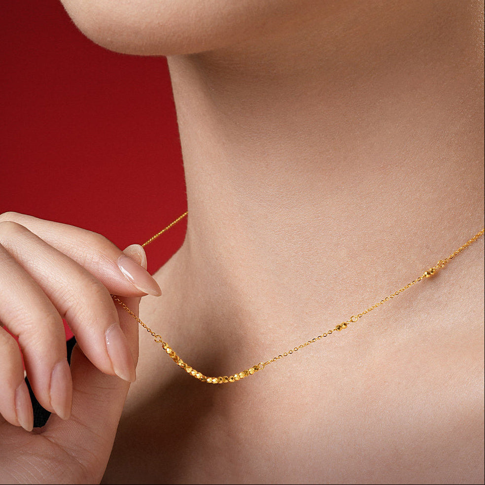 Woman holding 24K gold disco ball beaded necklace at collarbone on red background — close-up showing faceted gold bead sparkle and link chain detail