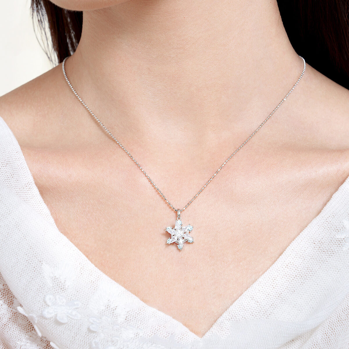 Model wearing ChowTaiSeng S925 silver snowflake necklace — rotating CZ pendant on box chain, white V-neck top, close-up front neck view