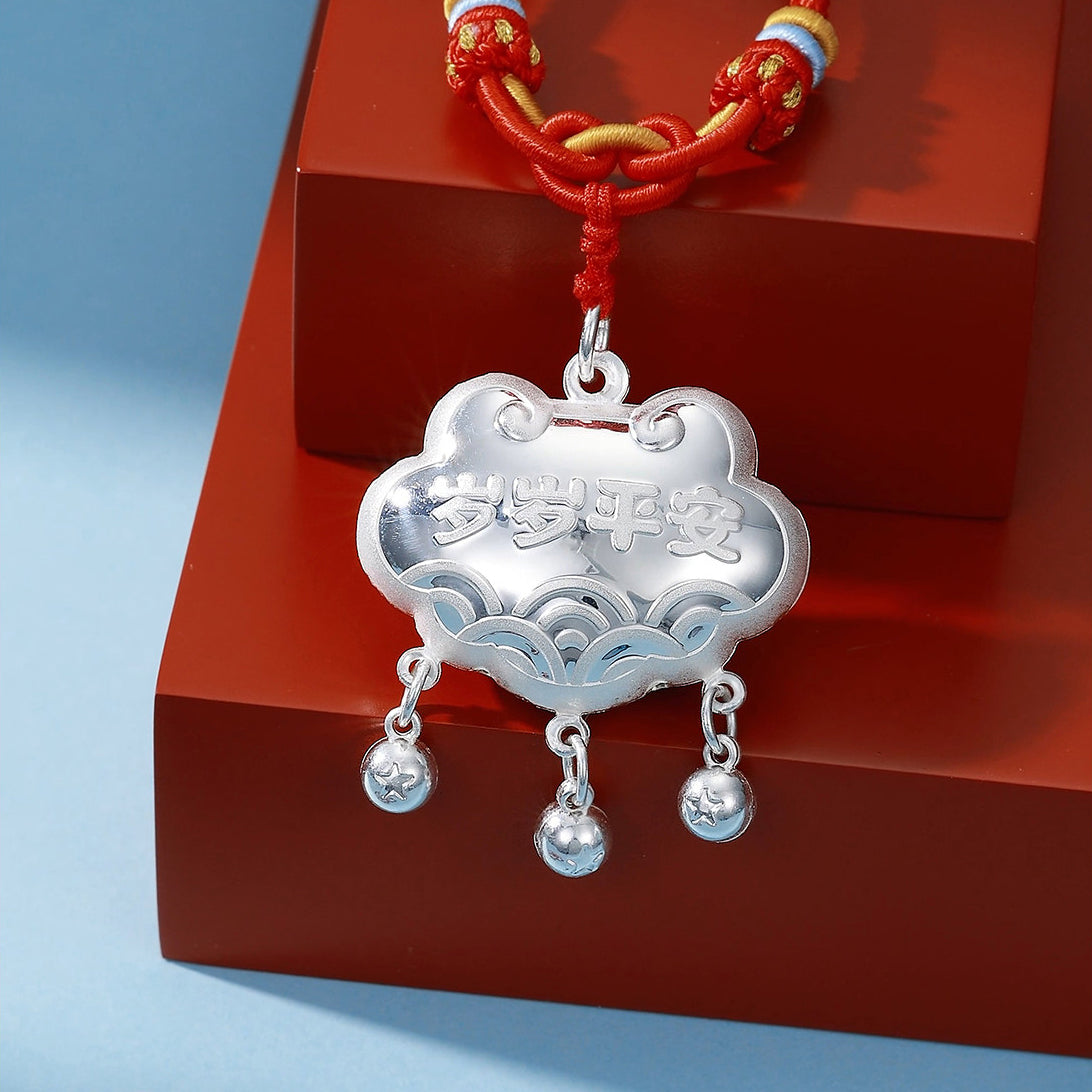 Back of 990 pure silver peace sheep Ruyi lock necklace on red wood surface — engraved Chinese blessing "岁岁平安" (Peace Year After Year) with wave pattern and three silver bell dangles