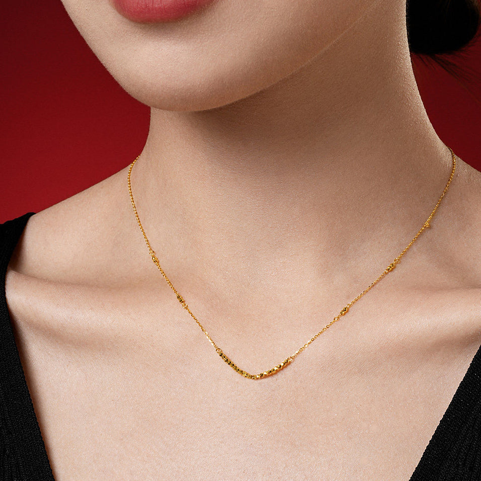 Model wearing 24K gold minimalist disco ball necklace on red background — faceted gold beads interspersed on fine link chain, elegant collarbone view