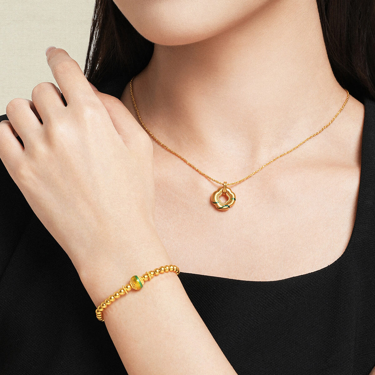 Model wearing ChowTaiSeng 24K Gold Green Clover Pendant necklace with matching 24K gold enamel bead bracelet, black top, lifestyle pairing shot