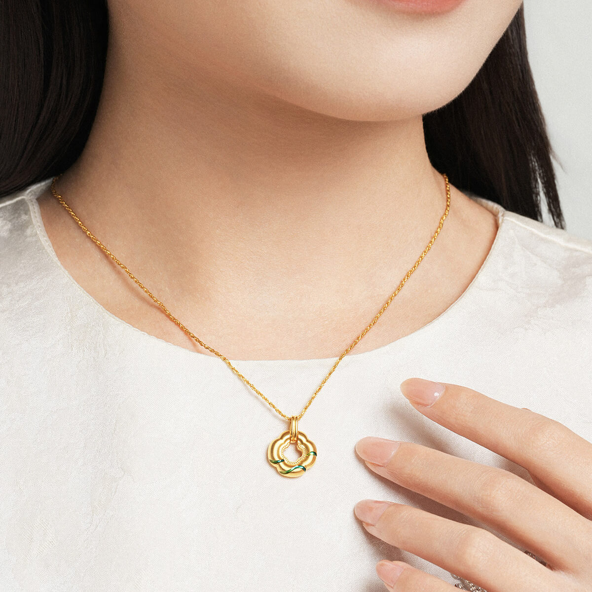 Model wearing ChowTaiSeng 24K Gold Green Clover Pendant on gold chain, white top, hand touching chest, elegant lifestyle shot
