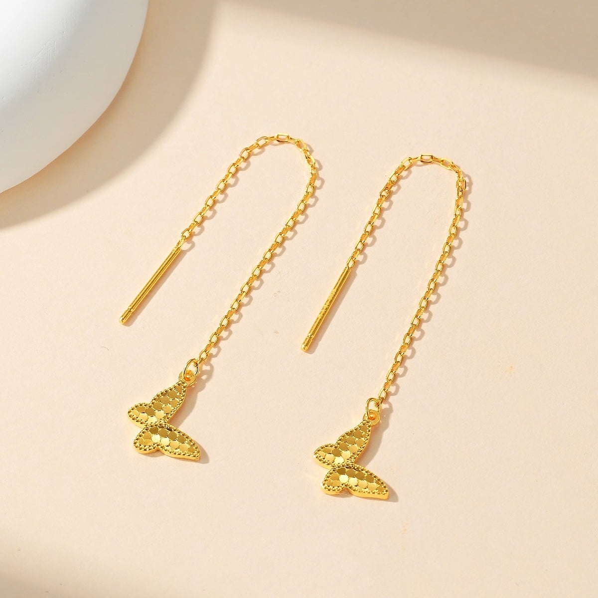 Gold-plated silver butterfly threader earrings with faceted wings on a cream display