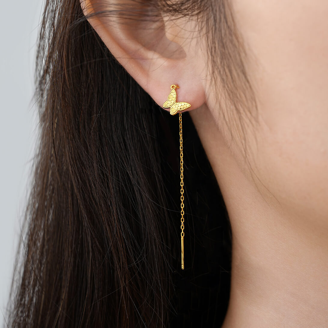 Gold-tone butterfly threader earring worn with the charm near the earlobe and a long chain drop behind