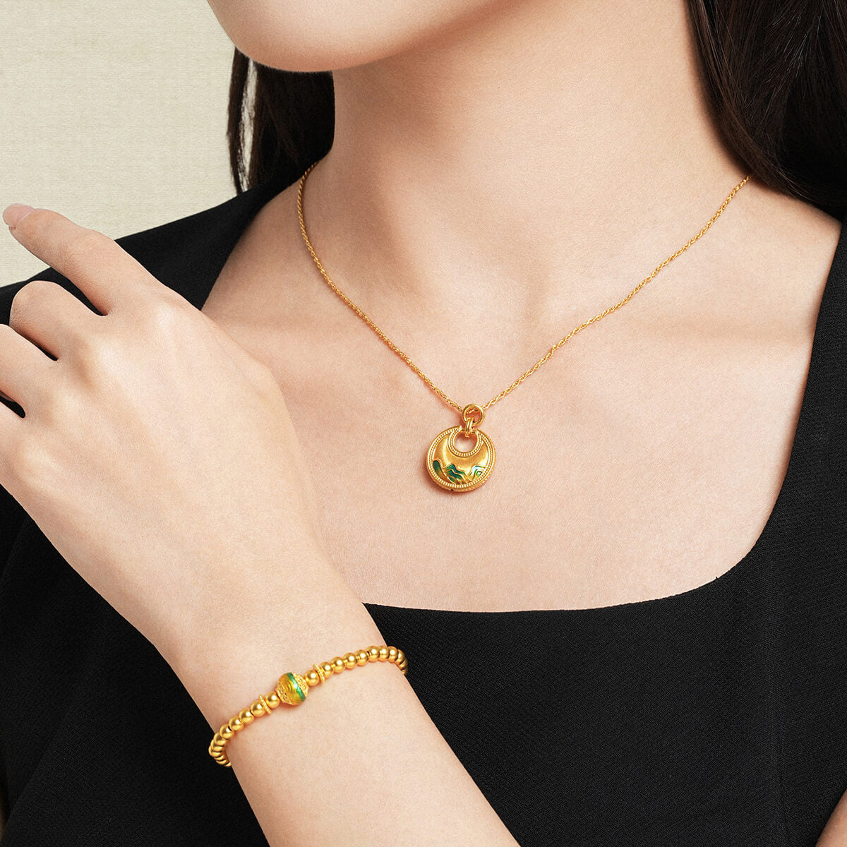 Model wearing ChowTaiSeng 24K Gold Round Ruyi Lock Pendant with matching enamel bead bracelet, black top, lifestyle pairing shot 