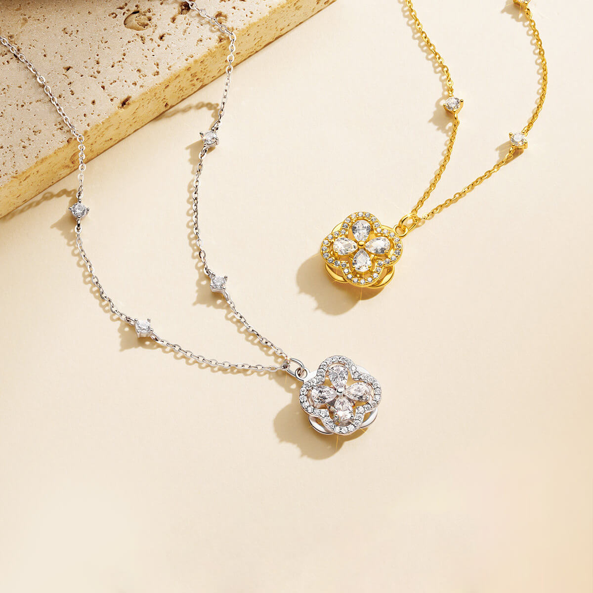 Silver-color and gold-tone clover necklaces with pear-cut cubic zirconia on a cream display beside stone