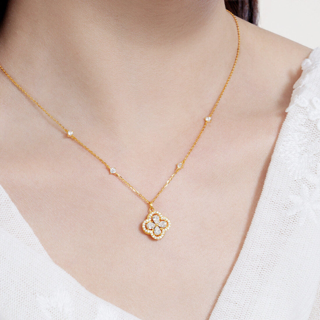 Model in a white top wearing a gold-tone clover necklace with clear cubic zirconia and a station chain
