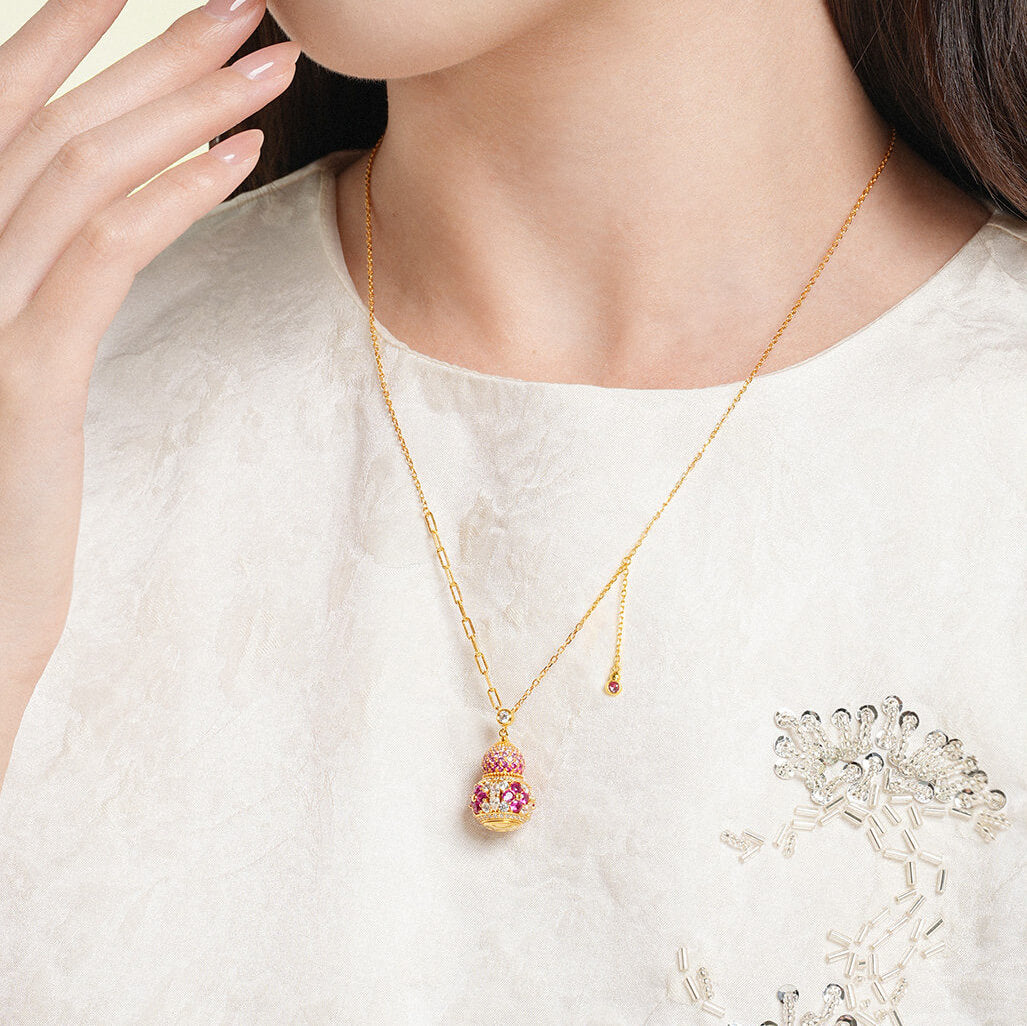 Model wearing a gold-plated silver gourd pendant necklace with an asymmetric chain over a white embroidered top