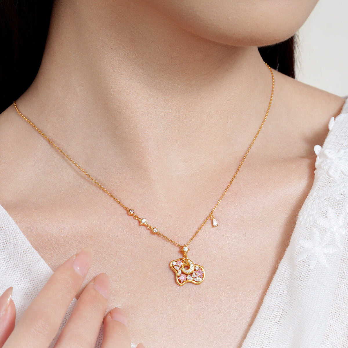 Close-up of a model wearing a gold-tone sheep necklace with pink cubic zirconia stars and a white textured top