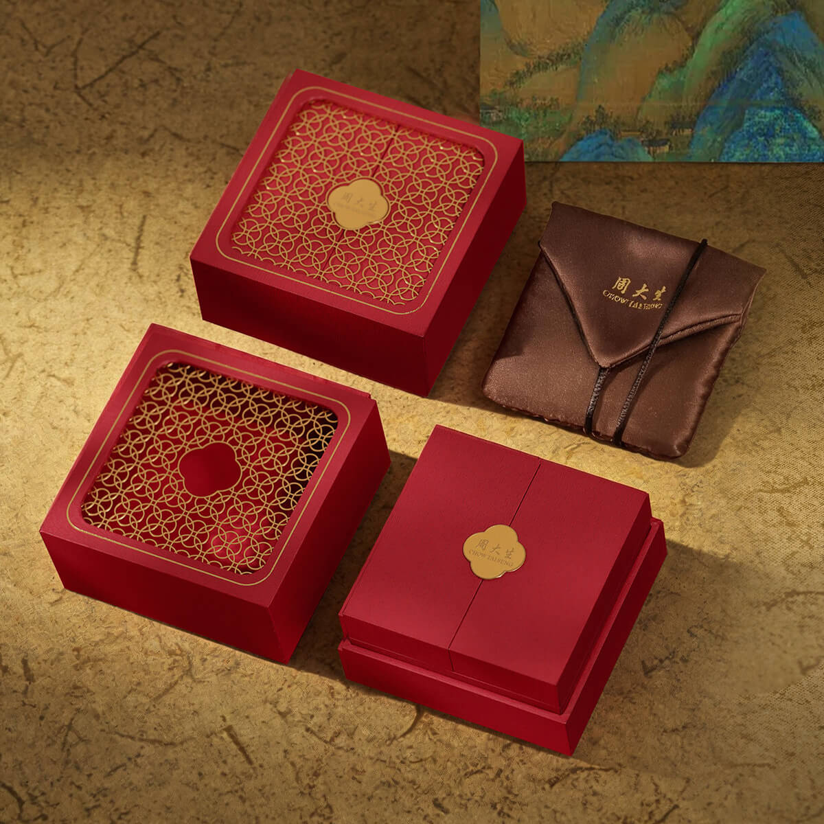 ChowTaiSeng luxury red gift box set with clover motif lid, brown silk pouch, and A Thousand Miles of Rivers and Mountains painting backdrop – premium jewelry packaging
